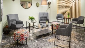 A modern interior with a marble floor, grey upholstered chairs, a glass coffee table, and a wooden staircase. - Hotel El Greco (Thessaloniki)