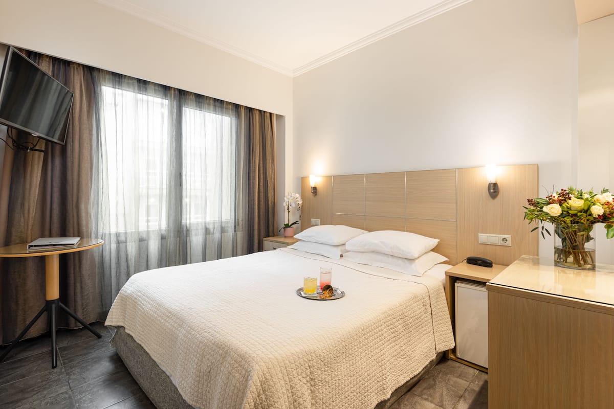 A hotel room with a large bed, bedside tables, a TV, and a small desk with a lamp.