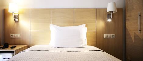A hotel room with a bed, bedside lamps, a nightstand, and a wooden wardrobe.