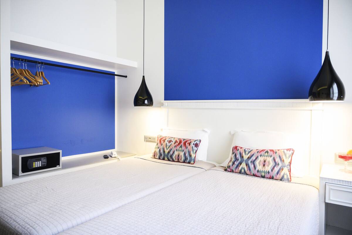 A hotel room with a large bed, a bedside table, a wall-mounted TV, and a wardrobe with hanging clothes.