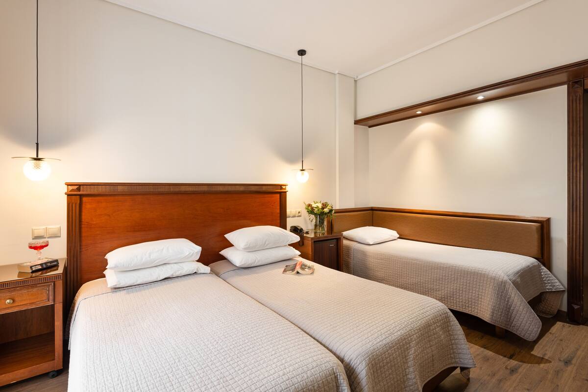 A hotel room with two beds, wooden headboards, and a nightstand with a lamp and a vase of flowers.