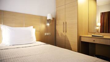 Habitación de hotel con cama, armario de madera, lámpara de noche y un pequeño escritorio con lámpara.