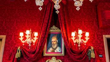 A luxurious room with a large bed, ornate chandelier, and a portrait on the wall.