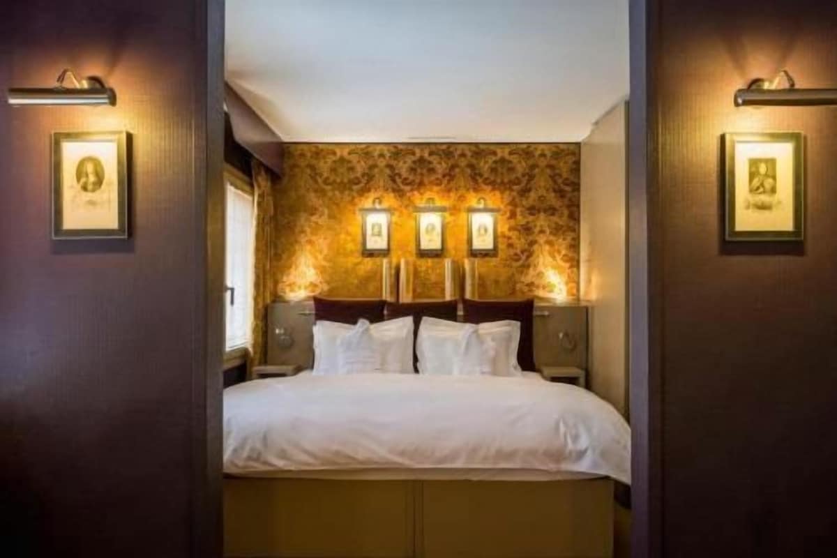 Een hotelkamer met een bed, wandlampen en ingelijste foto's.