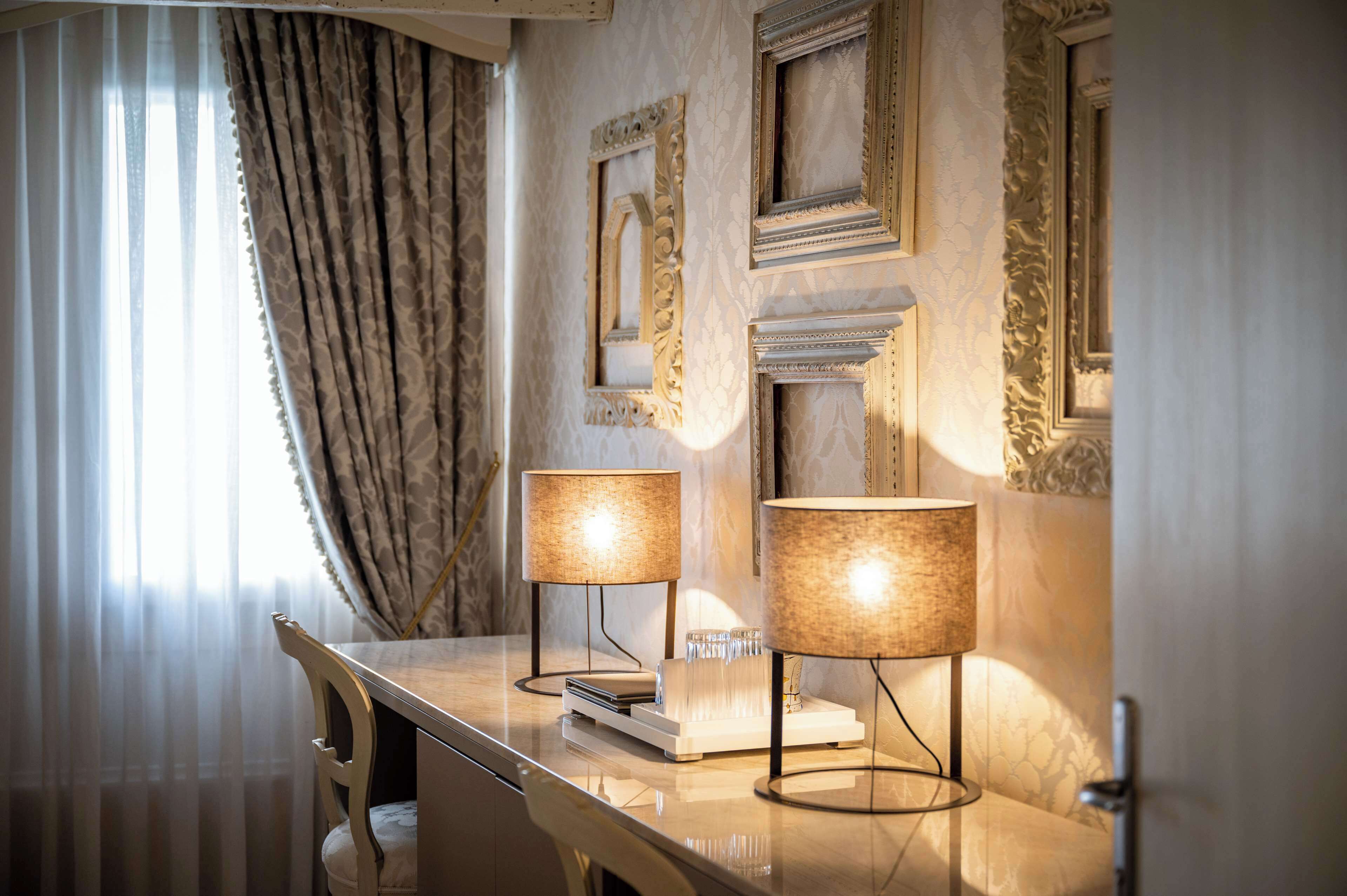 Une chambre d’hôtel avec un bureau en marbre, deux lampes et des miroirs encadrés accrochés au mur.
