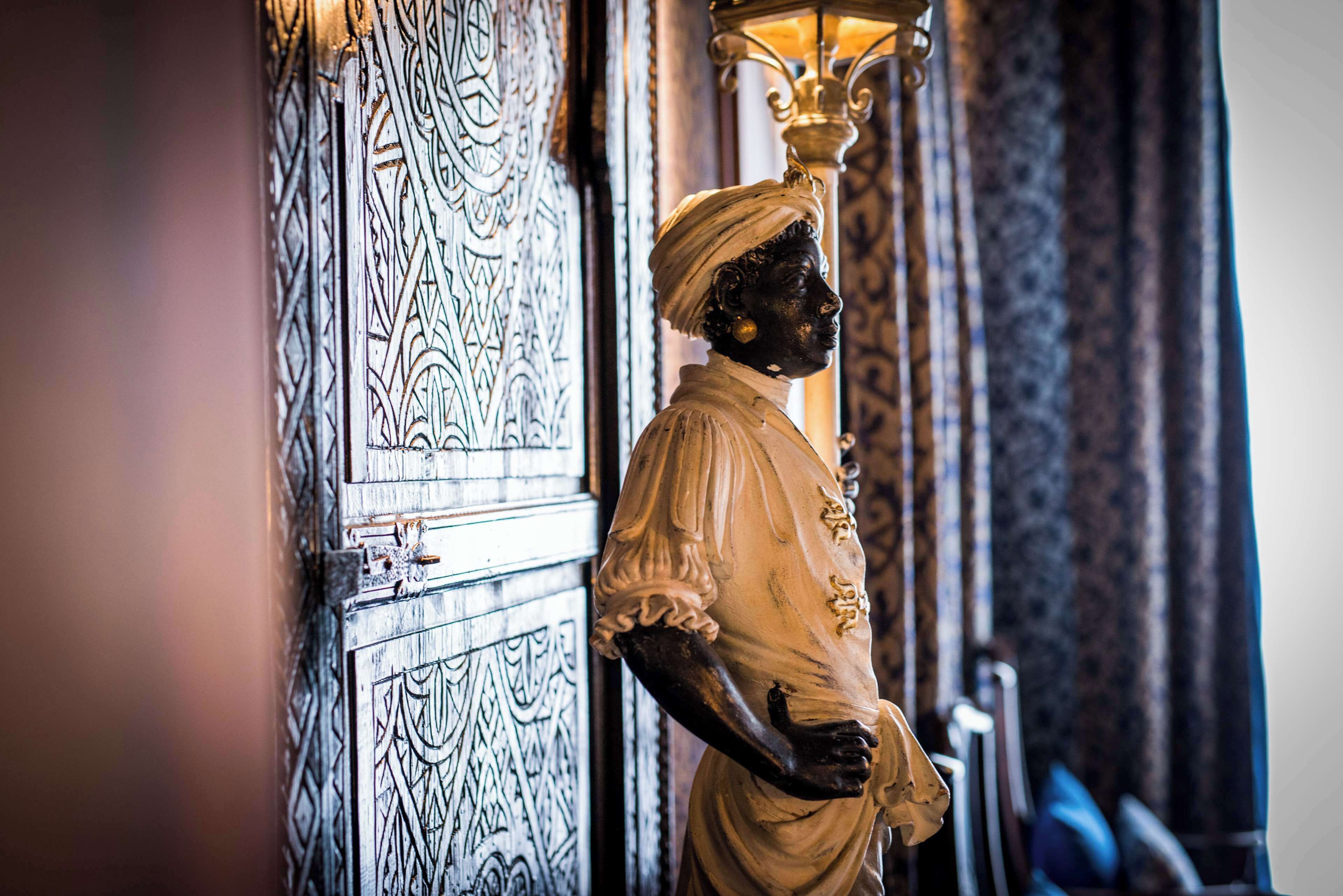 Una estatua en una habitación con puertas ornamentadas y una cortina estampada.