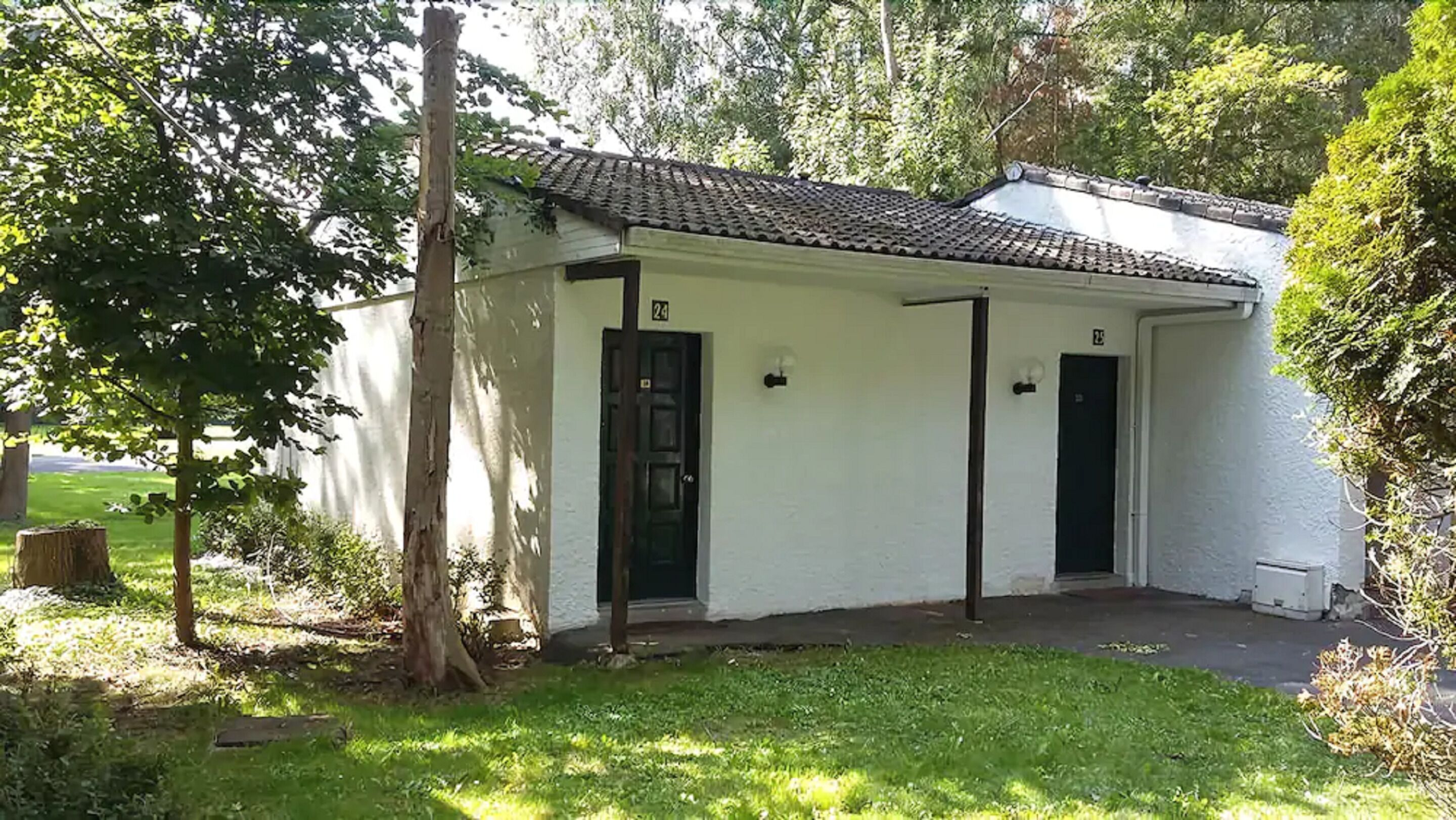 A small, single-story building with a tiled roof, two doors, and a small porch area.