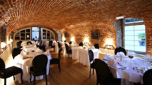 Een restaurant met bakstenen muren en gewelfde plafonds, tafels gedekt met witte tafelkleden en stoelen.