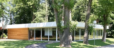 A modern building with a wooden facade and large glass windows, surrounded by trees and a paved walkway.
