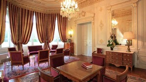 Een luxueuze kamer met versierde plafond- en wanddecoraties, een kroonluchter en een grote spiegel.