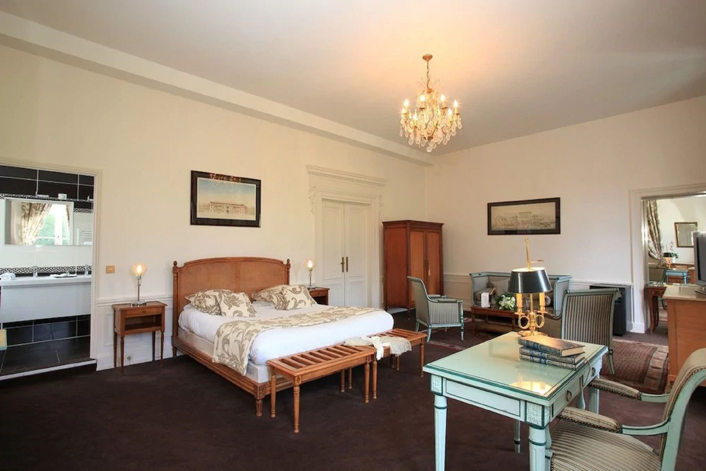 A bedroom with a large bed, a desk with a lamp, a chair, and a mirror.