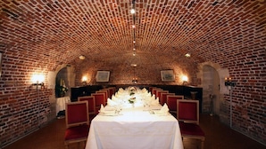 Een feestzaal met een bakstenen plafond, witte tafellaken en rode stoelen.