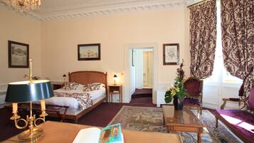 A hotel room with a bed, a desk with a lamp, a chair, a sofa, and a large window with curtains.