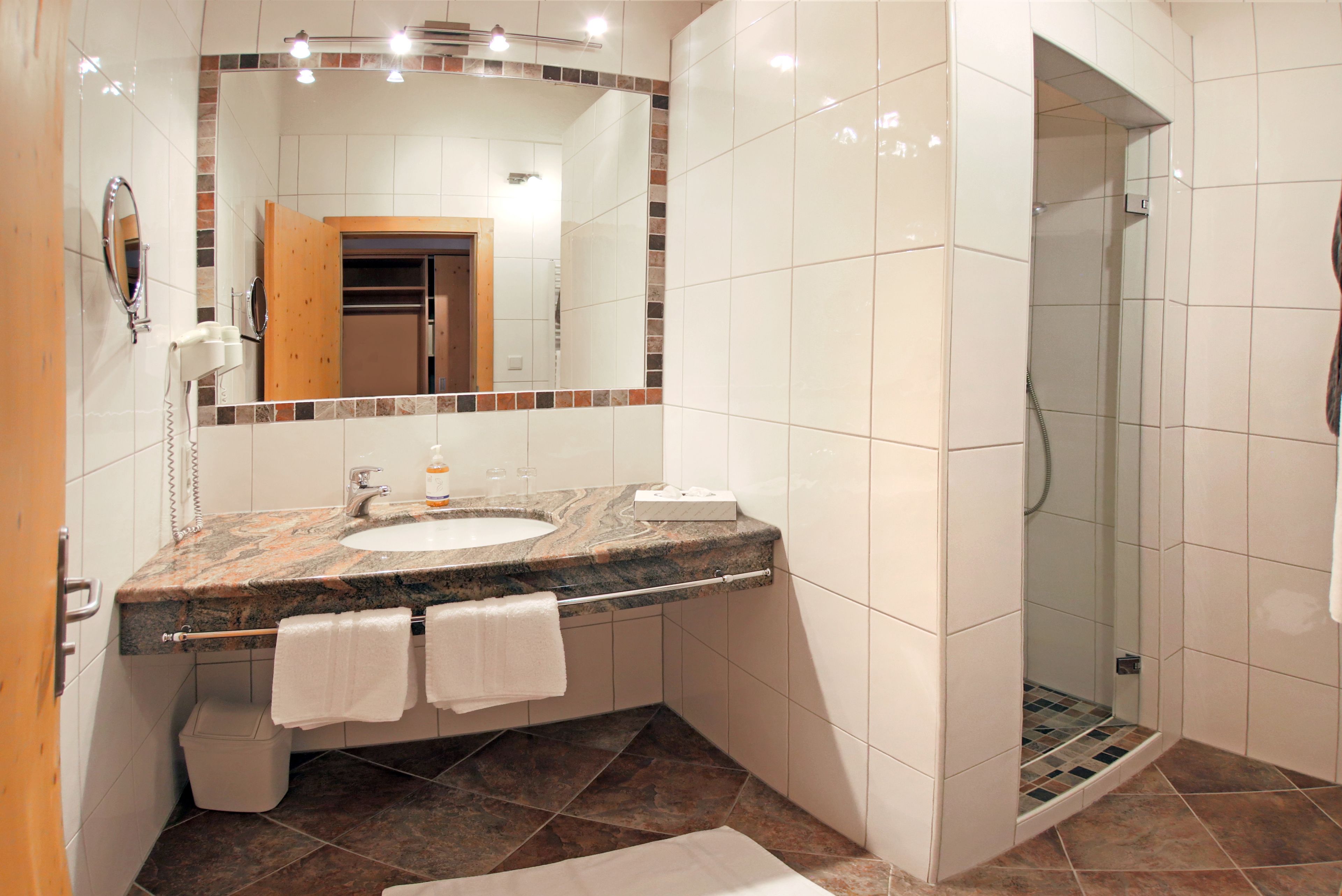 Une salle de bain avec un lavabo en marbre, un grand miroir, une douche et un sol carrelé.