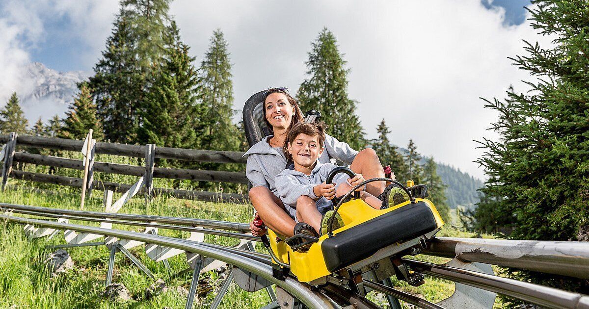A person riding a yellow vehicle on a metal track surrounded by greenery and trees.