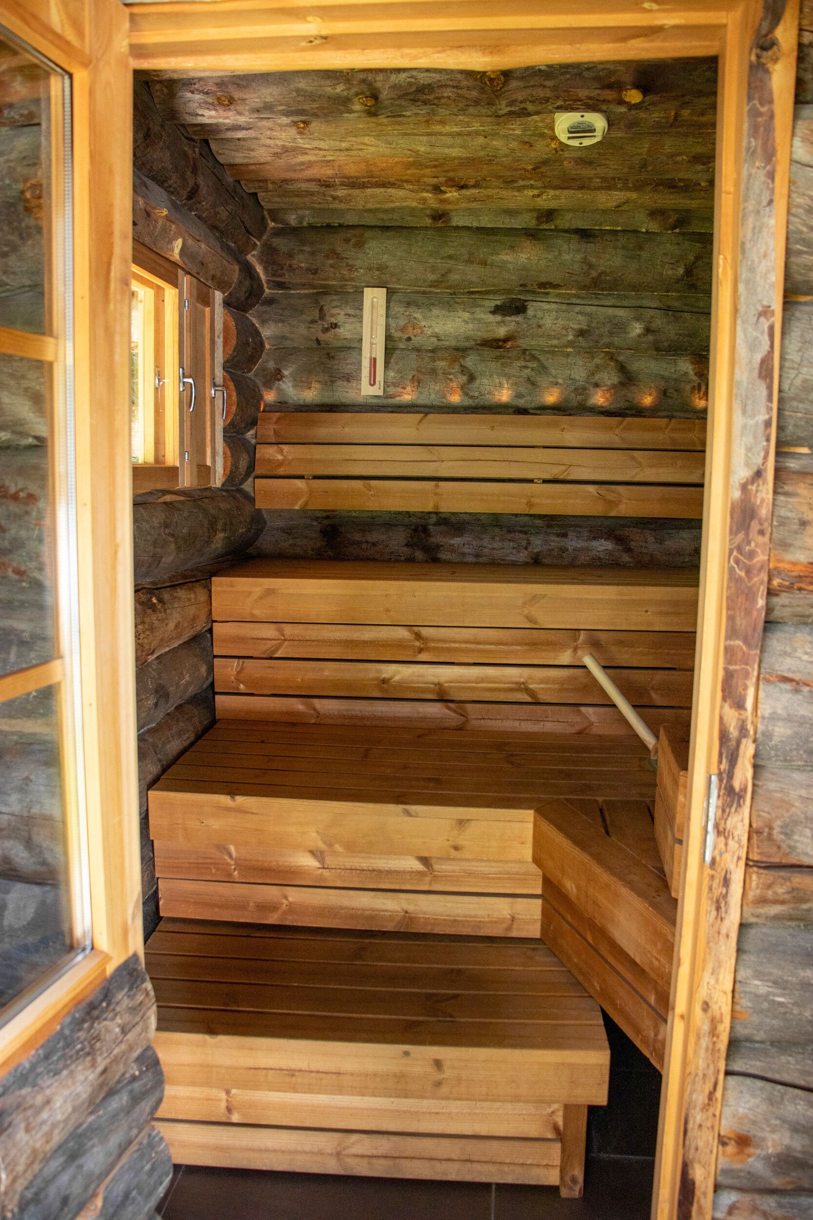 A wooden sauna with a wooden bench and a thermometer on the wall.