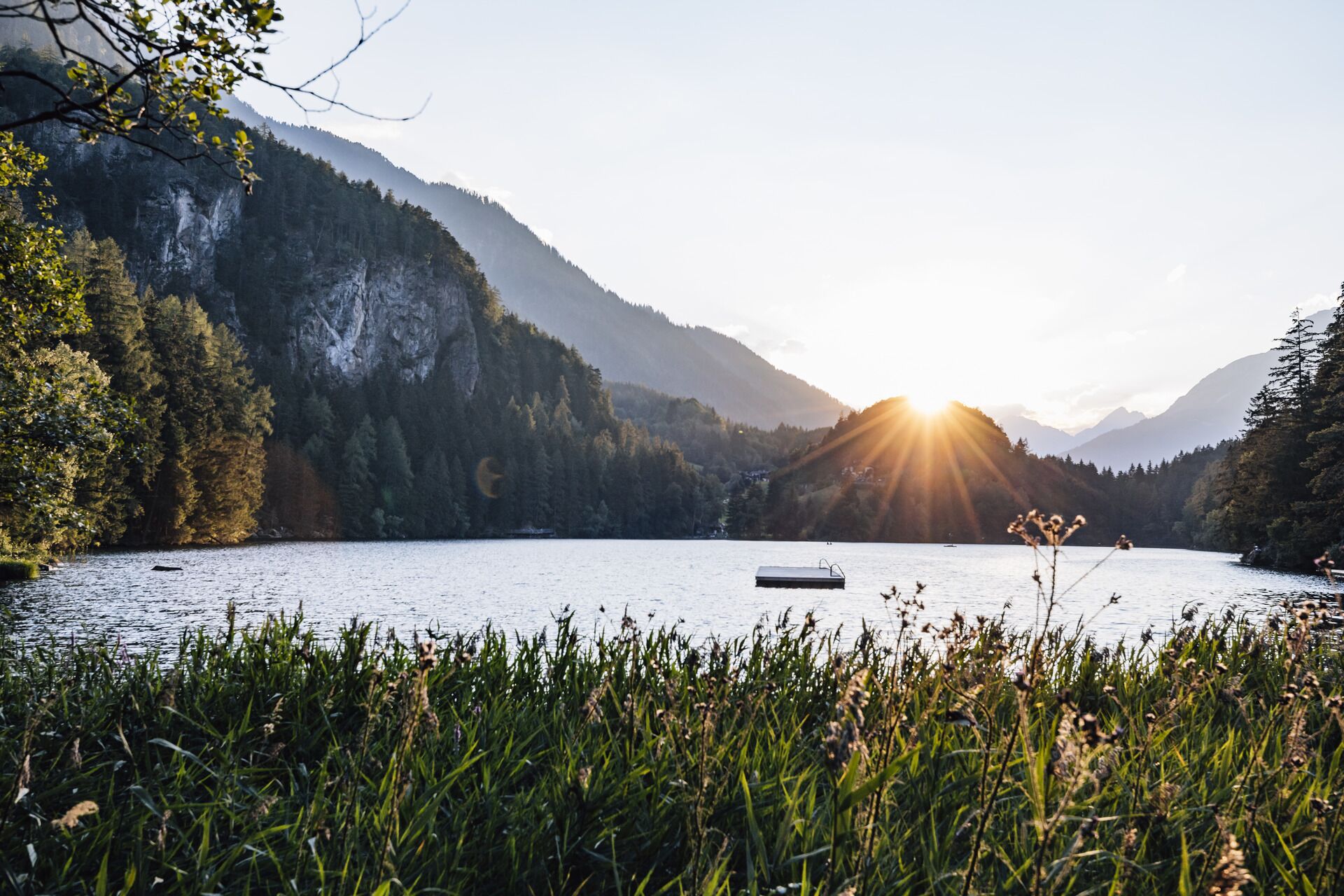 A serene lake surrounded by forested mountains with a wooden dock extending into the water.