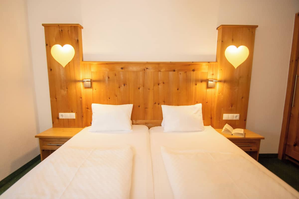 A double bed with a wooden headboard, two bedside tables, and two wall-mounted light fixtures shaped like hearts.