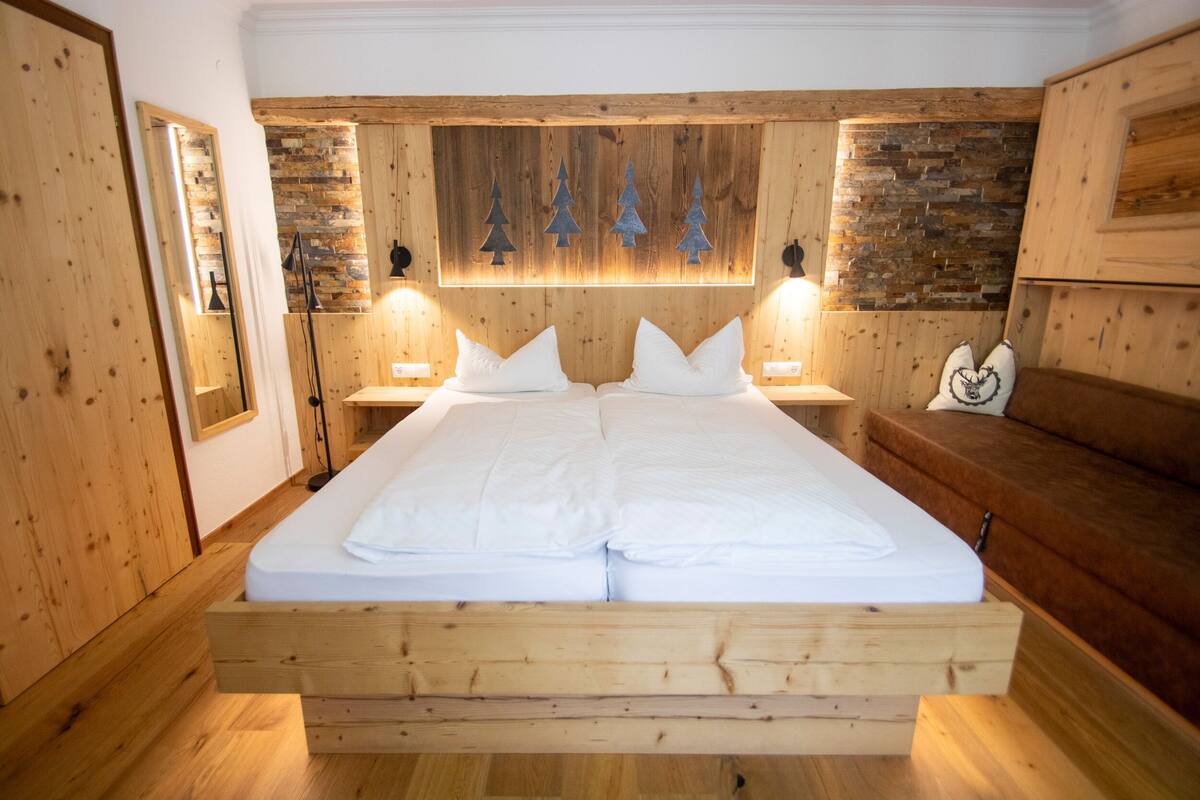 A wooden-framed bed with white bedding, wooden walls, and a brick accent wall with Christmas tree decorations.