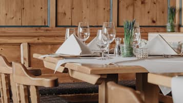 Een houten eettafel gedekt met witte servetten, wijnglazen en een kleine potplant.