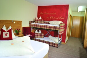 A hotel room with a bunk bed, a single bed, and a red accent wall with German text.