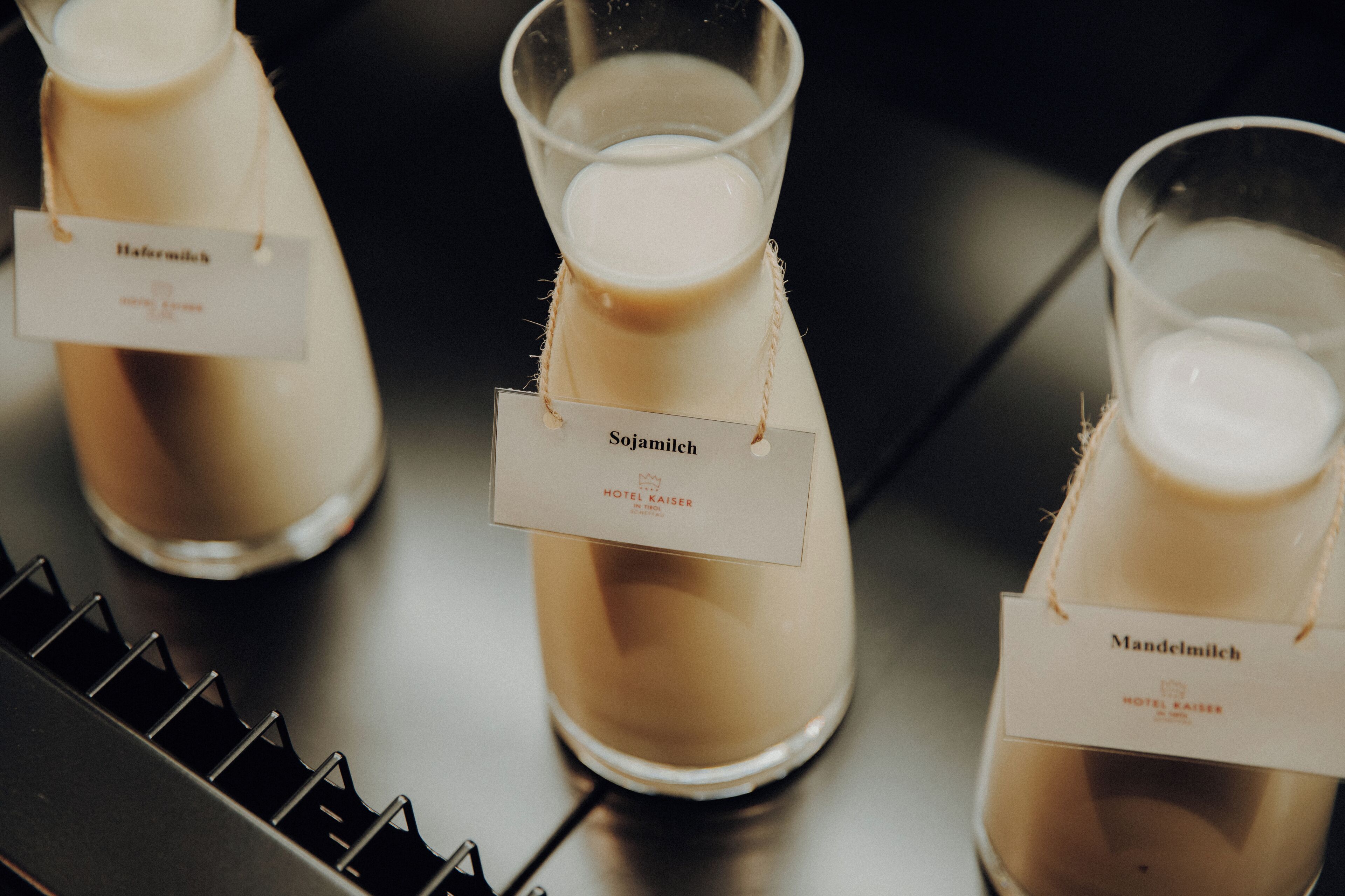 Three bottles of milk labeled 'Sojamilch' and 'Mandelmilch' with tags, placed on a black surface.
