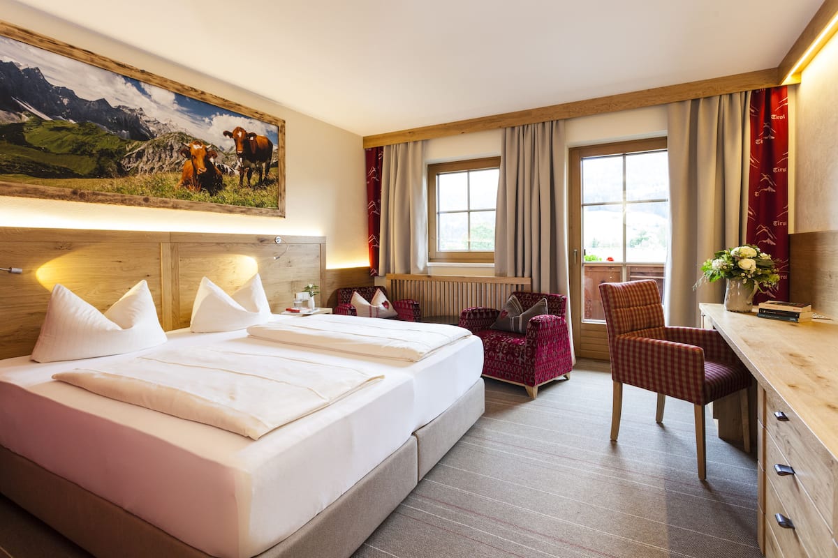 A hotel room with a large bed, two bedside tables, a desk, a chair, and a window with curtains.