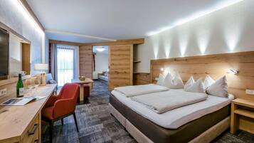 A hotel room with a large bed, a desk with a chair, a TV, and a window with curtains.