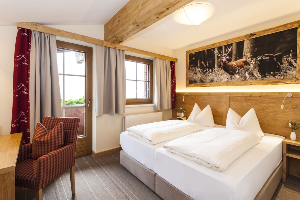 A hotel room with a bed, a chair, a window, and a painting on the wall.