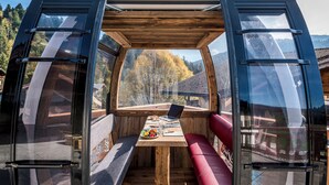 A compact, open-plan room with a wooden table, a laptop, and a red bench. - Hotel Kaiser in Tirol (Scheffau am Wilden Kaiser)