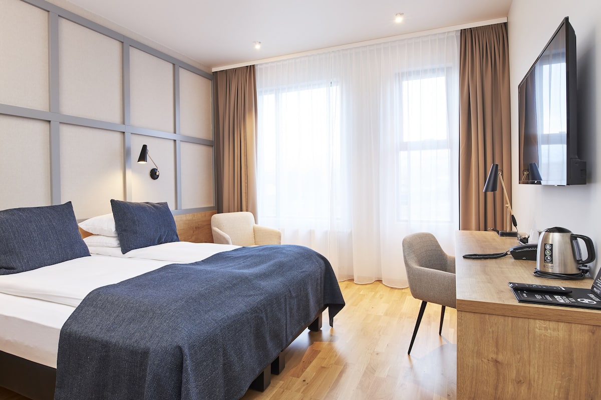A hotel room with a bed, a desk, a chair, a television, and a coffee maker.