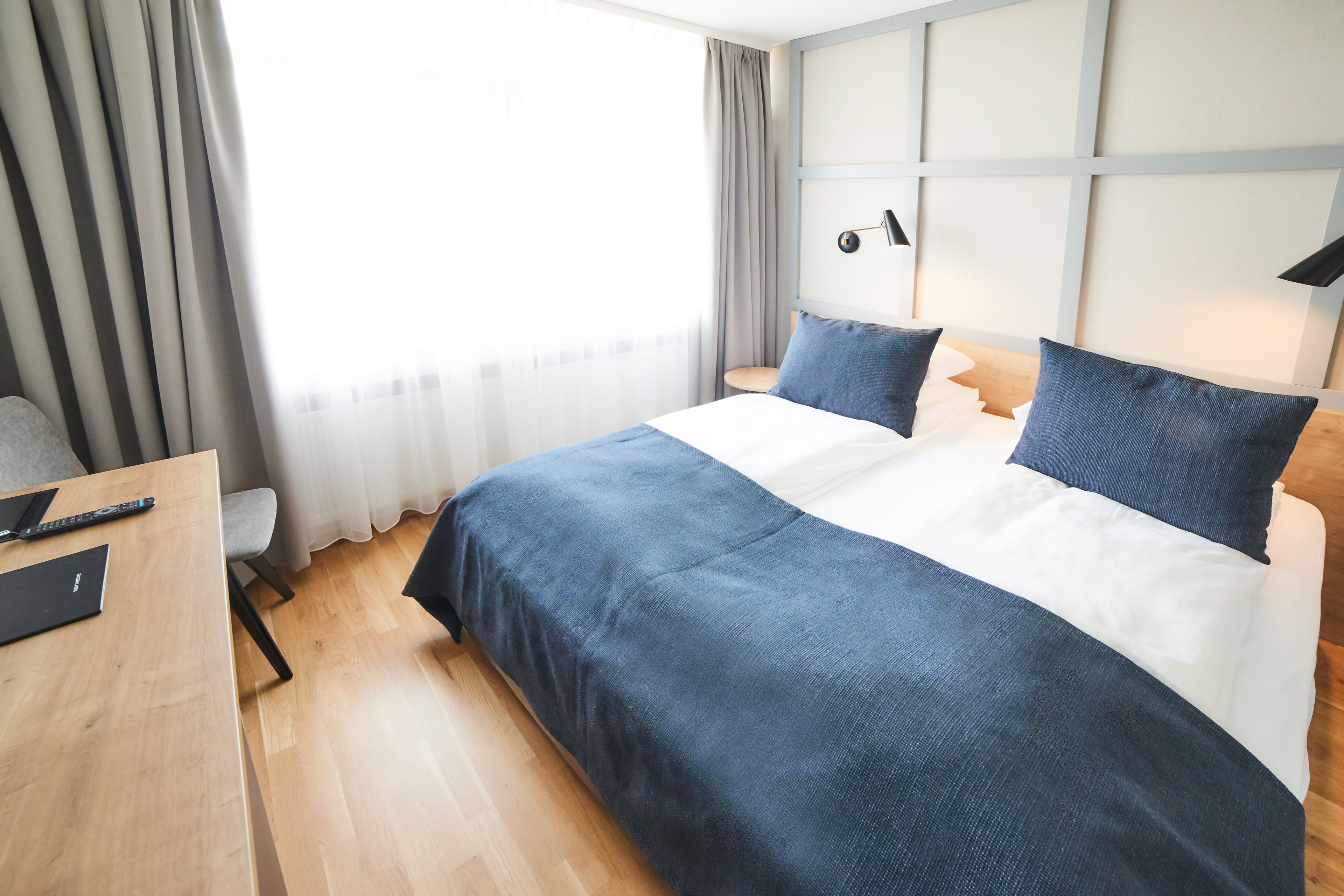 A hotel room with a bed, a desk, a chair, and a window with curtains.