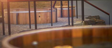 A wooden hot tub with metal railings, a stone-paved area, and a rustic setting.