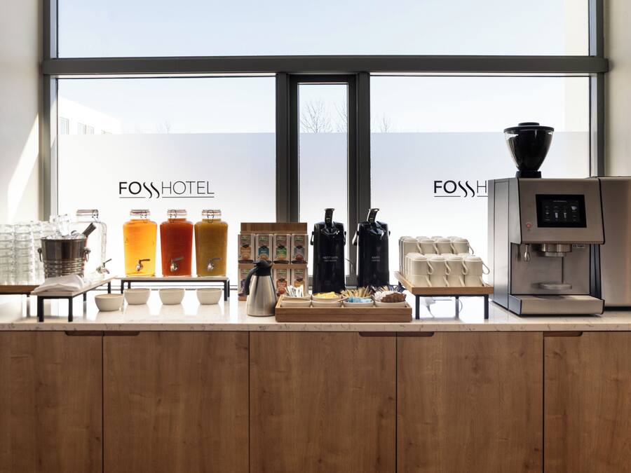 Zona de recepción de hotel con máquina de café, estación de té y varios dispensadores de bebidas.