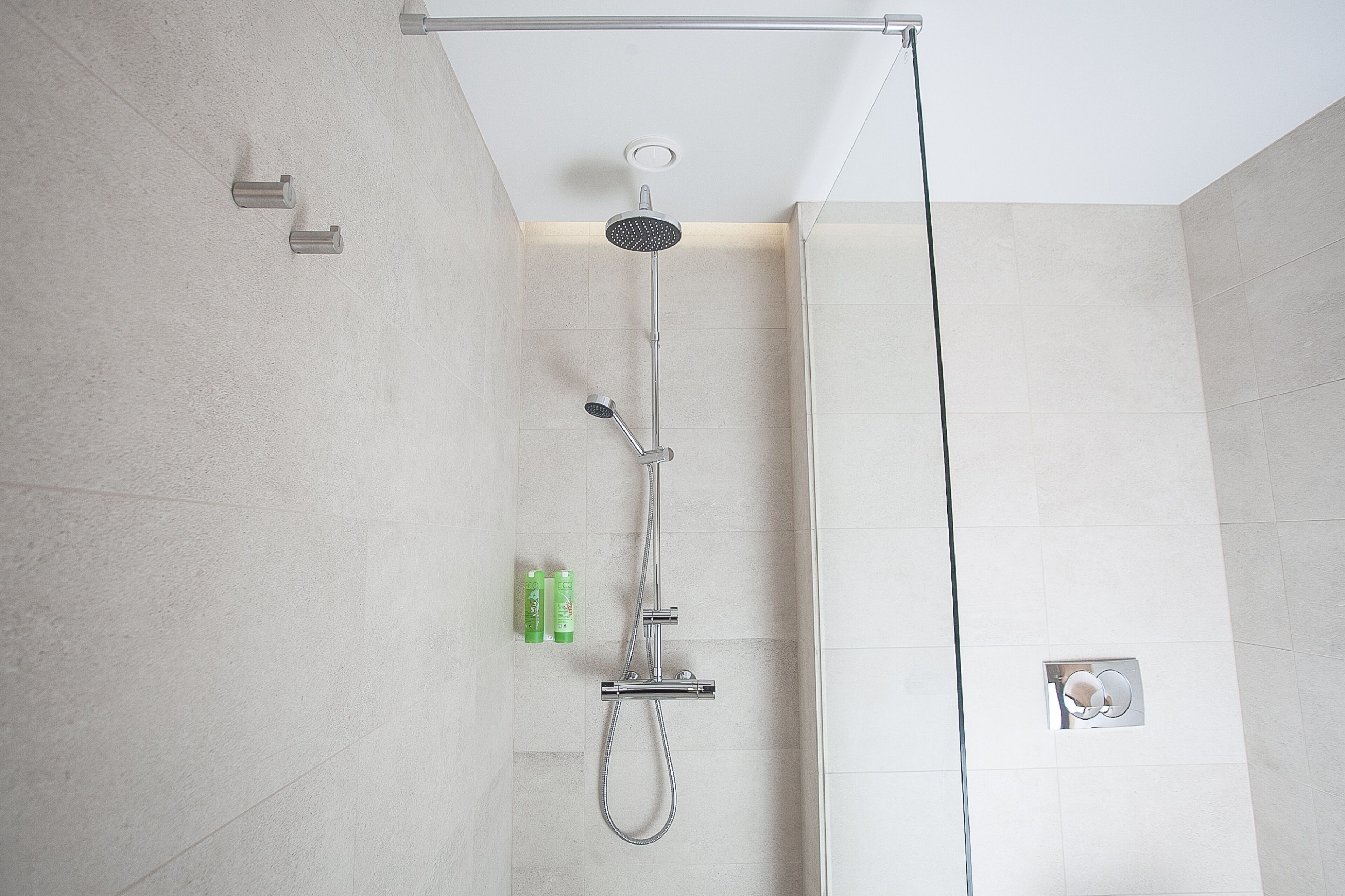 A modern shower with a handheld showerhead and a fixed showerhead, a handheld shower attachment, and a wall-mounted control panel.
