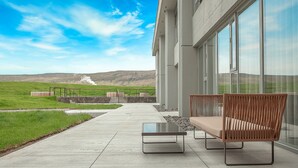 A modern outdoor seating area with a glass table and bench, overlooking a grassy field and distant hills. - Fosshotel Reykholt (Borgarbyggd)