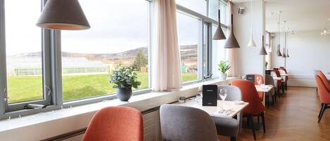 Un espace repas moderne doté de grandes fenêtres, de plusieurs tables et de chaises.