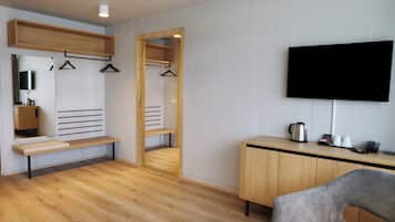 Ein modernes Zimmer mit einer Holzbank, einem an der Wand montierten Fernseher, einem Spiegel und einem Schrank mit Wasserkocher und Tassen.