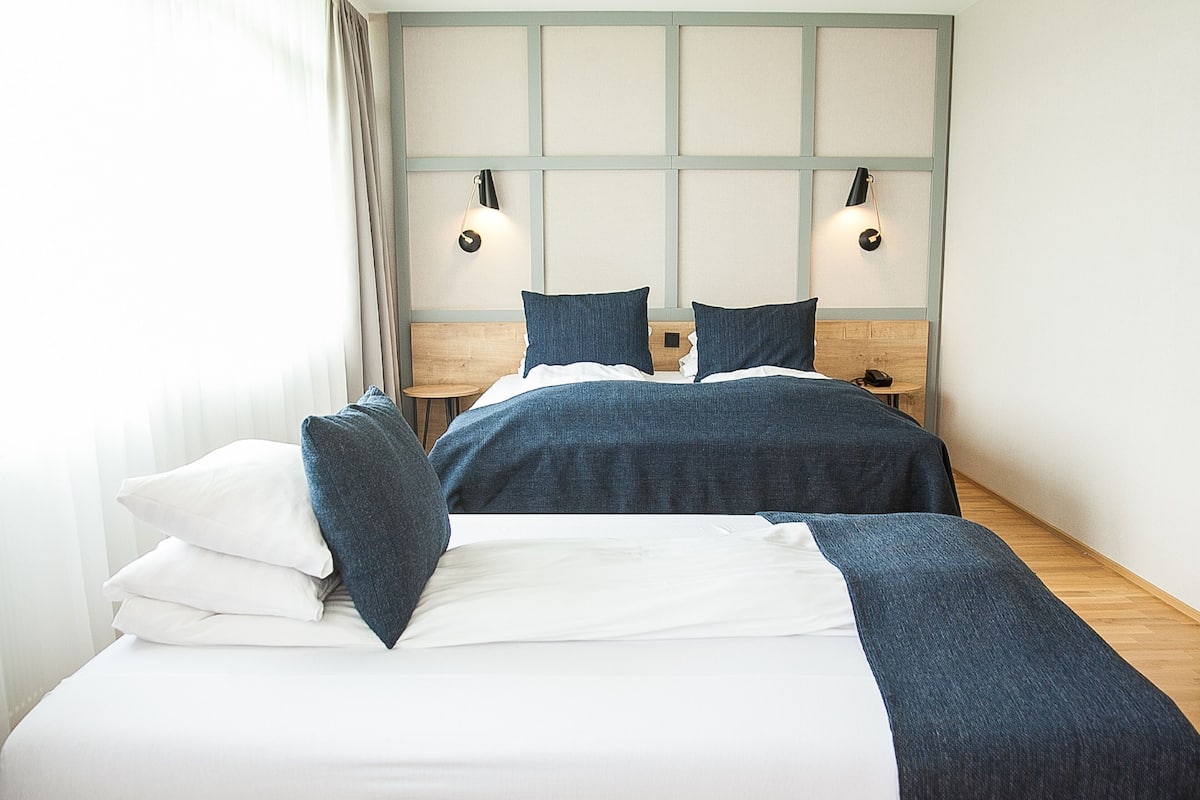 A neatly made bed with a wooden headboard, two bedside tables, and two wall-mounted lamps.
