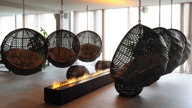 A modern interior with hanging wicker chairs and a central fire feature. - Fosshotel Reykholt (Borgarbyggd)