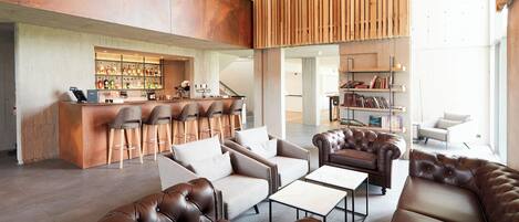 A modern lounge area with leather sofas, a bar, and a bookshelf.