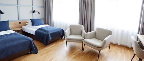 A hotel room with two beds, a desk, and two chairs.