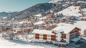 Estância de montanha coberta de neve com vários edifícios em estilo chalé, um teleférico e uma vista clara da paisagem nevada ao redor.