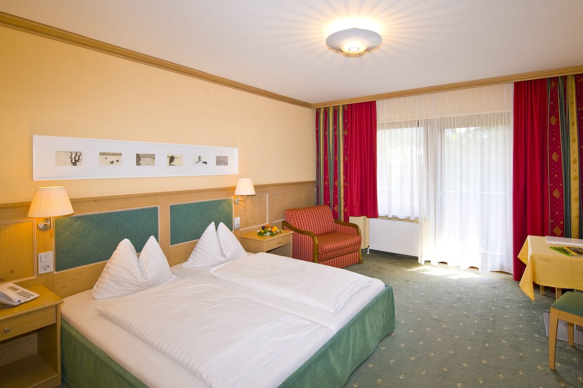 A hotel room with a large bed, two bedside tables, a desk, a chair, and a window with curtains.