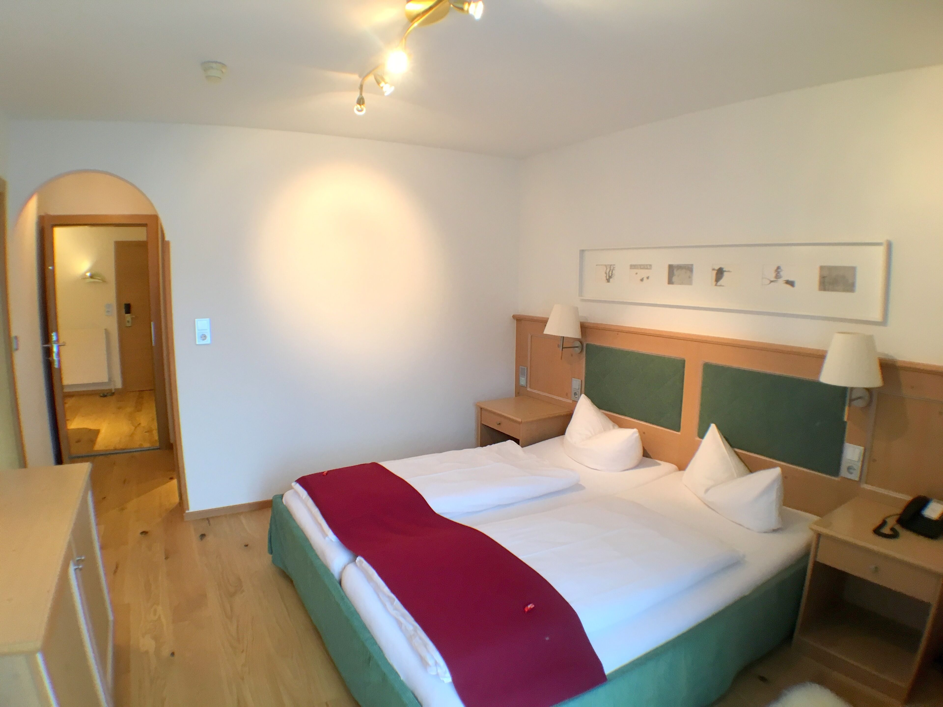 A hotel room with a large bed, a wooden headboard, bedside lamps, a small table, and a framed picture on the wall.