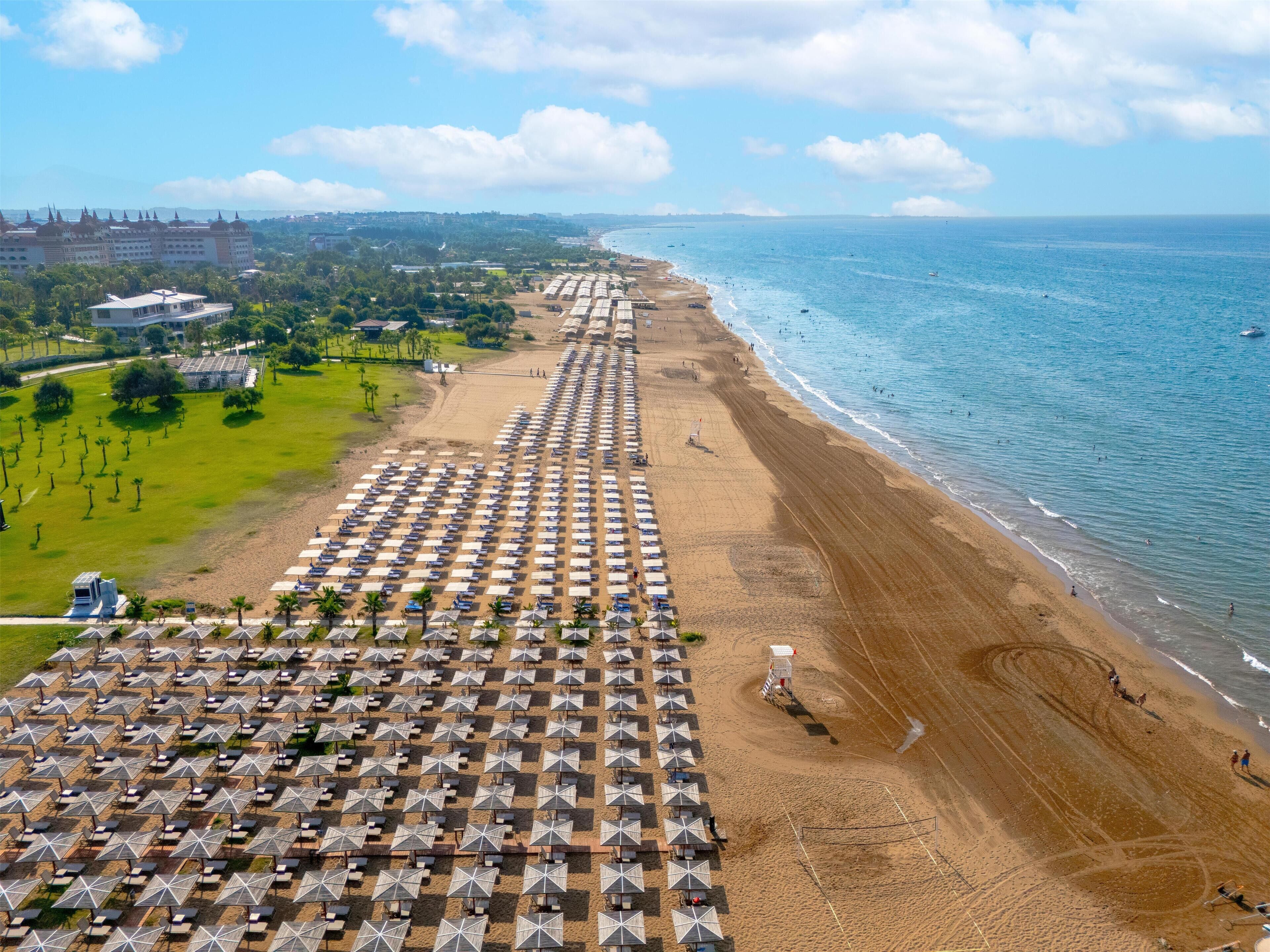 A beach with rows of umbrellas and beach chairs, a lifeguard tower, and a hotel in the background.