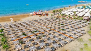 A beach with numerous sun umbrellas and lounge chairs arranged in rows, a lifeguard tower, and a building with a sign that reads "After Sports Center". - Sural Saray Hotel - All inclusive (Manavgat)