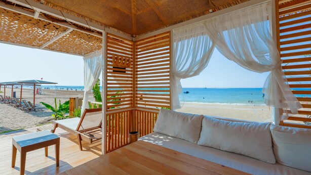 A beachside room with a wooden floor, a sofa with white cushions, a small table, and a view of the beach and ocean. - Sural Saray Hotel - All inclusive (Manavgat)