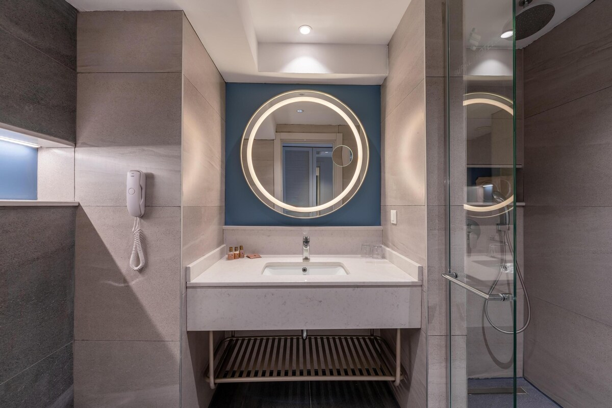 A modern bathroom with a large mirror, a white sink, and a glass-enclosed shower.