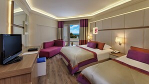 Habitación de hotel con dos camas, televisión, escritorio y vista al exterior.